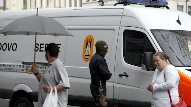 People walk past a bomb squad van outside Antwerp Central train station in Antwerp, Belgium on Saturday when homes and car ports were searched in 16 municipalities in an anti-terror sweep.