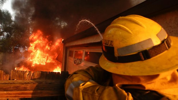 A Los Angeles County firefighter puts water on a burning house in the Lake View Terrace area of Los Angeles.