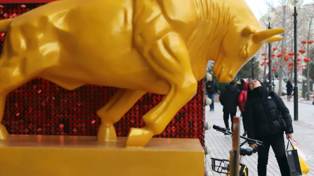 A woman looks up near a sculpture of a golden bull in Beijing, China.