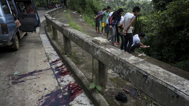 Blood stains the roadside as  civilians view unidentified bodies believed to have been executed and dumped in a ditch by militants. 