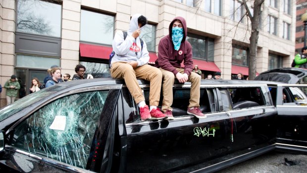 Demonstrators sit on top of a limousine with the windows broken during the demonstration in downtown Washington on Inauguration Day.