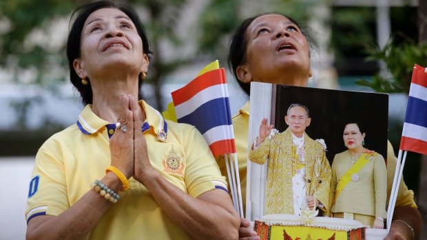 Thais hold portraits of King Bhumibol Adulyadej and Queen Sirikit as they pray outside the Grand Palace during the  70th anniversary of the king's accession to the throne in June.