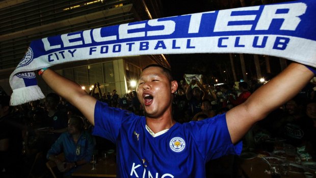 A Leicester City fan holds up a club scarf at the headquarters of the King Power duty free company.