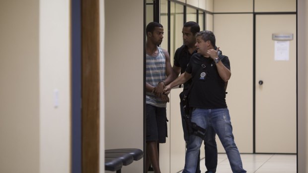 Rai de Souza, 22, a gang rape suspect is escorted by officers to the police headquarters in Rio de Janeiro.