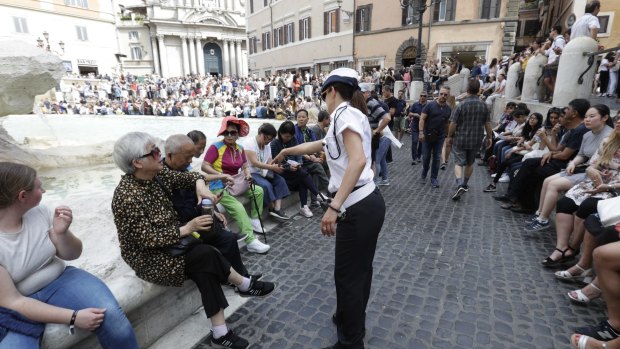 A police officer talks to tourists gathered in front of Trevi fountain.