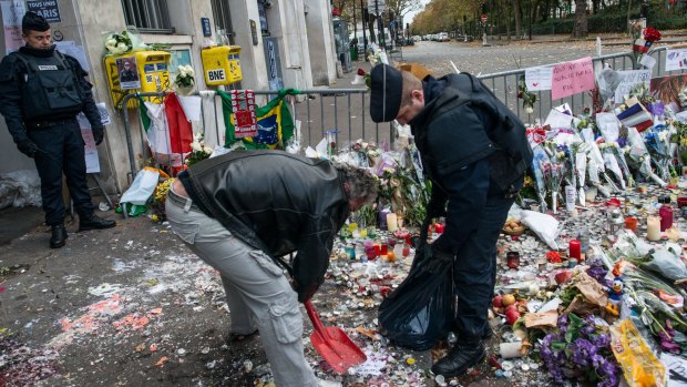 Police officers remove candles and flowers from the front of the Bataclan concert hall.