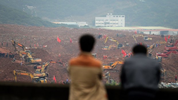 People watch rescuers using machinery to search for potential survivors following the landslide in Shenzhen.