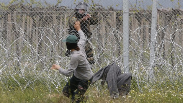A Macedonian police officer takes aim at a migrant who had been trying to remove barbed wire along the border with Greece.