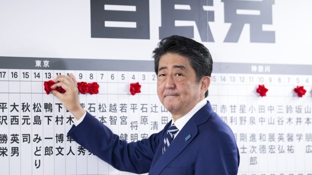 Japanese PM Shinzo Abe places a red paper rose on a LDP candidate's name to indicate a lower house election victory at the party's headquarters in Tokyo on Sunday.