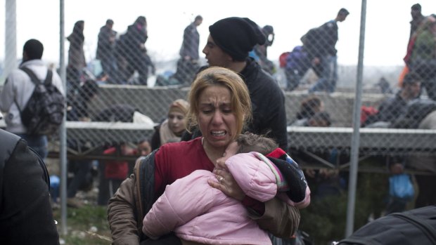 A woman carries a child on the Greek side of the border as they run away after Macedonian police fired tear gas at a group trying to push their way into Macedonia, from Idomeni in Greece.