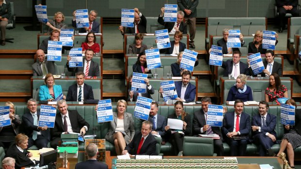 Labor MPs hold up signs on school funding during question time.