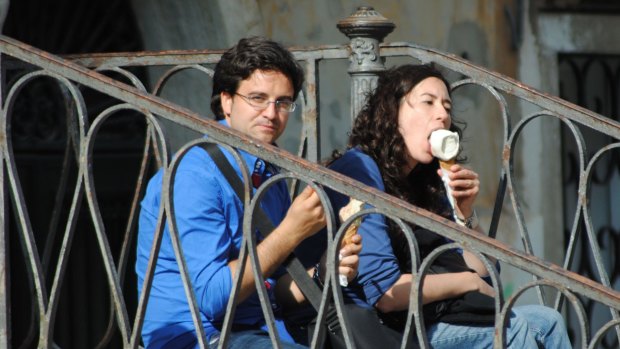 Tourists eat ice creams, sitting on a bridge in Venice.