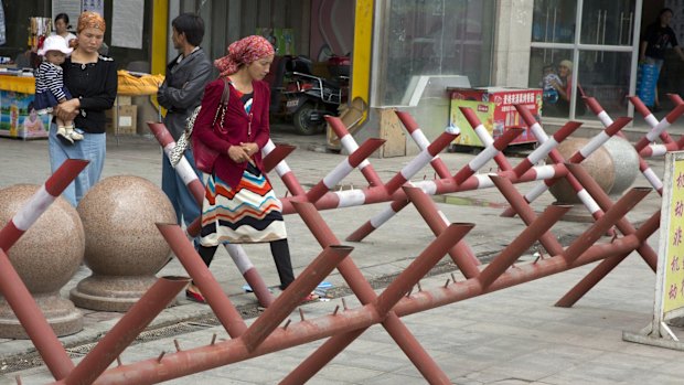 Uighur women walk past barricades set up at the entrance to a shopping district in the city of Aksu in western China's Xinjiang province in 2014.