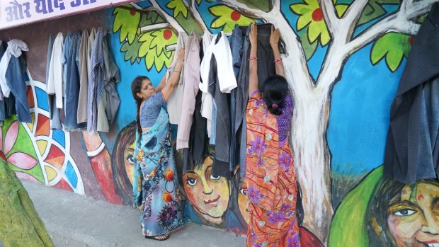 Women hang donated clothes on the wall that is giving locals a taste for charity.