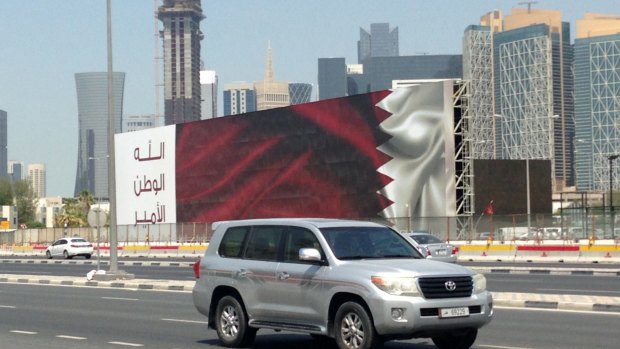 An SUV drives past a billboard featuring the Qatari flag and the slogan "God, Nation, Emir" in Doha.