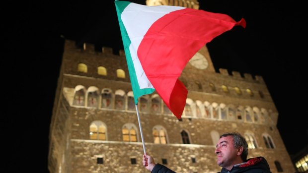 A 'Yes' campaign supporter waves the Italian national flag in Piazza della Signoria before Matteo Renzi speech.