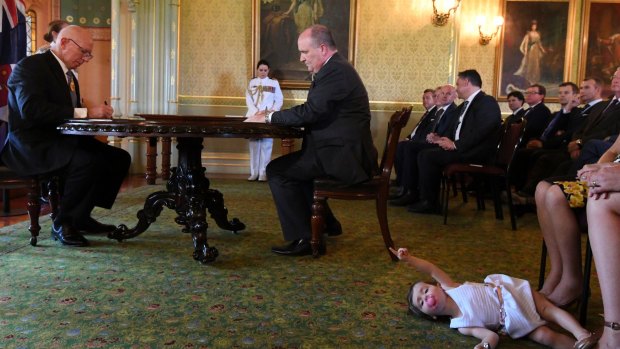 David Elliott, new Minister for Counter Terrorism, signs an oath at Government House as John Barilaro's daughter Sofia plays at her mother's feet.