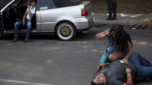 A woman talks on a phone over a wounded Edgar Osvaldo Vega, as Pedro Gracias sits in a car bleeding, after being shot by unknown gunmen while driving near Caleta beach in Acapulco, Mexico. 