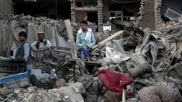 Men sit amid debris of their properties at the site of a truck bomb blast in Kabul on Friday.