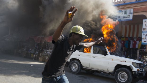 A protester runs past a burning car during a demonstration to demand the cancellation of the run-off elections in Port-au-Prince, Haiti.