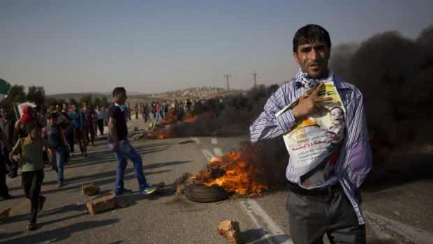 A Palestinian demonstrator holds up a photo of slain toddler Ali Dawabshe during clashes at the entrance to the village of Duma.