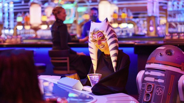 A passenger wearing a Togruta headpiece sits at the holo-sabacc table in the Sublight Lounge onboard the Halcyon starcruiser.