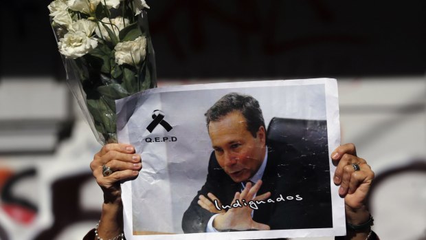 A woman holds up flowers and an image of late prosecutor Alberto Nisman while waiting for the hearse with his remains, in Buenos Aires January 29, 2015.