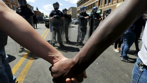People hold hands in front of police officers in riot gear outside a looted and burned store in Baltimore on Tuesday.