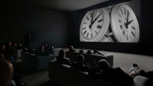 An audience watches <i>The Clock</I>, which for some viewers it is strangely melancholic, a memento mori showing how inexorably time is passing.