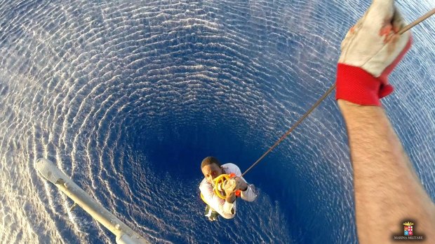 A migrant is lifted on board by an helicopter from the Italian Navy ship Orione, after he and another migrant were spotted clinging to a barrel, in the Mediterranean Sea, between Libya and Italy on August 11. 