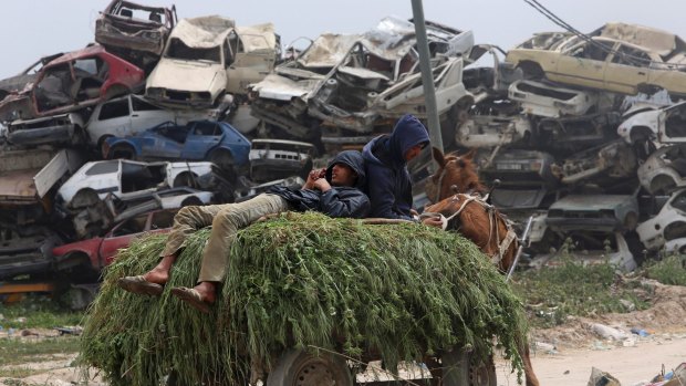 Farmers rest on a horse cart loaded with animal fodder as they pass a junkyard on their way to their barn, in  the Gaza Strip town of Beit Hanoun.