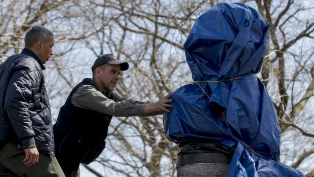 New York City Parks workers work to remove a covered large molded bust of Edward Snowden at Fort Greene Park in Brooklyn.