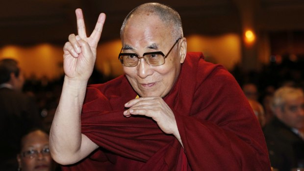 The Dalai Lama directs a peace sign towards the head table. 