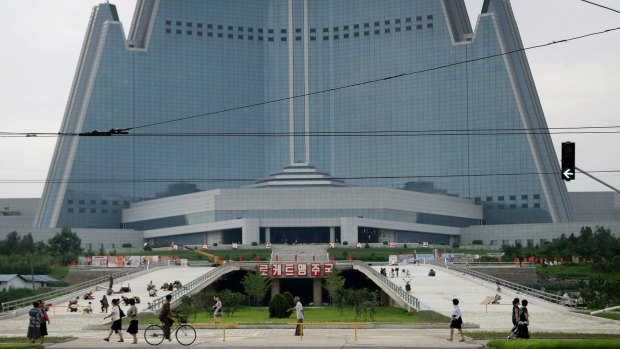 People walk past the under construction 105-storey pyramid shaped Ryugyong Hotel where men are seen working on a driveway.