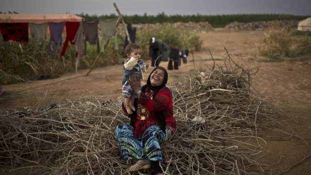 Syrian refugee Fatima Jassim, 40, plays with her 7-month-old daughter Marwa while sitting on a pile of wood to be used for cooking, outside their tent at an informal tented settlement near the Syrian border on the outskirts of Mafraq, Jordan, last month.