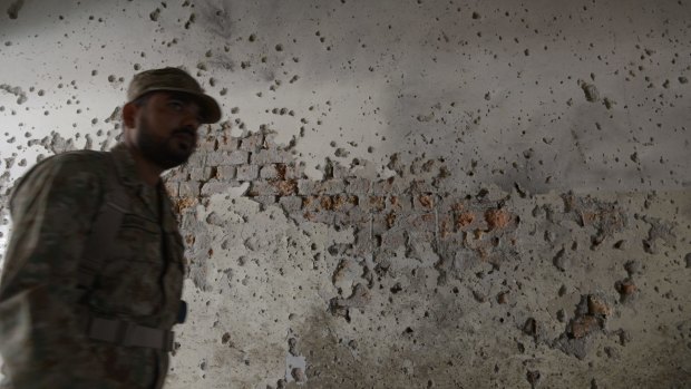 A Pakistani army soldier walks past a bullet-riddled wall.