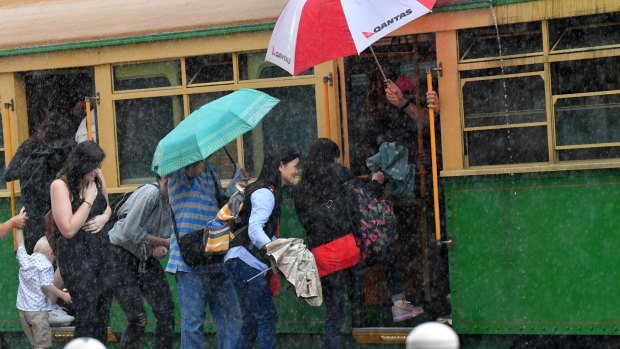 People scramble onto a tram as heavy rain hits the city.