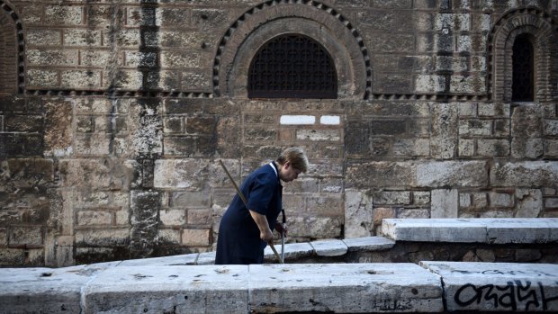 A worker cleans the sidewalk outside a Greek Orthodox church in Athens on Friday..