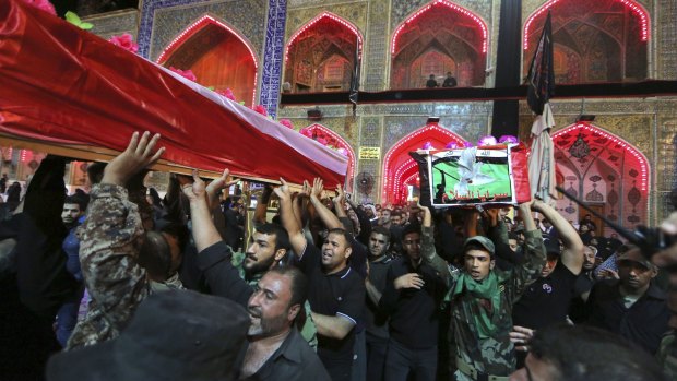 Mourners and militiamen chant slogans against the Islamic State group as they carry the flag-draped coffins of two members of the Peace Brigades, a Shiite militia group.