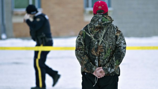A man holds a rosary as police investigate the scene of a shooting at the community school in La Loche, Saskatchewan.