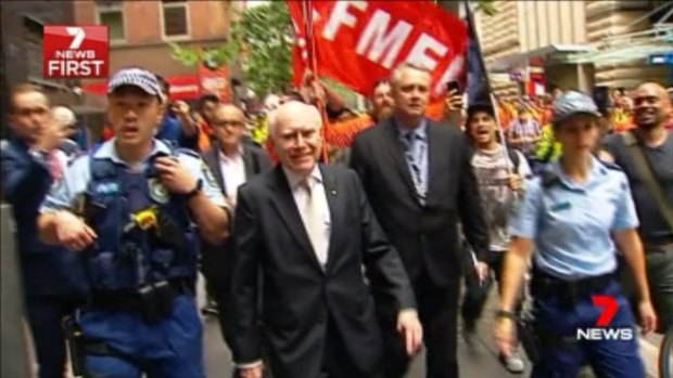 Former prime minister John Howard is escorted by police in Sydney.