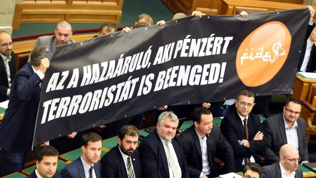 Members of the far-right opposition Jobbik party hold a banner which reads: "The traitor is the one who lets the terrorist in for money!", complete with pseudo-Arabic script, during the vote.