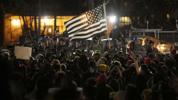 Protesters raise a flag as they confront the police outside the Ferguson Police Department. 