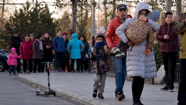 A woman carries a child as they arrive at the RYB kindergarten in Beijing, China, on Friday.