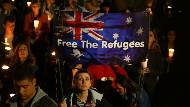 People hold candles and signs up in support of refugees at a Light The Dark rally in Sydney.