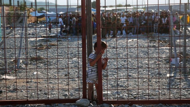 A young Iraqi boy slips through a narrow opening in a gate inside a camp used for temporary detention of migrants shortly after they crossed the Macedonian border from Greece.