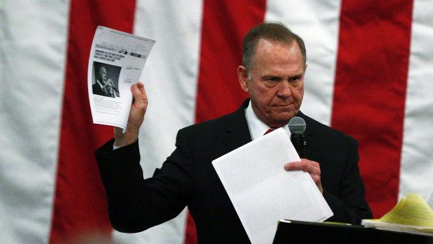 US Senate candidate Roy Moore holds up pages with a news story about himself at a campaign rally on Monday.
