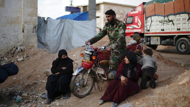 A Syrian soldier passes by Syrian women displaced with their families from eastern Aleppo.