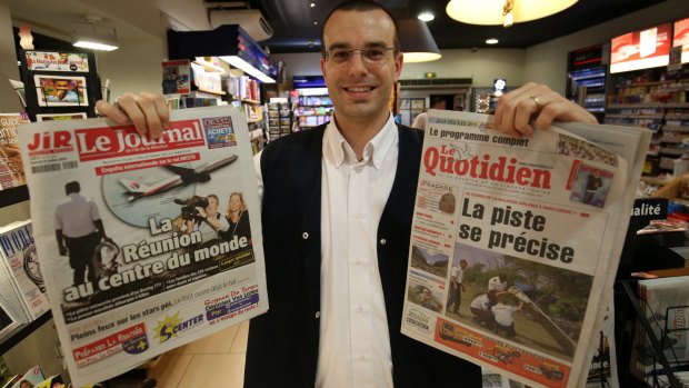 Saint-Denis newsagent owner Frederik Varin holds up the front pages of two local newspapers covering the MH370 story.