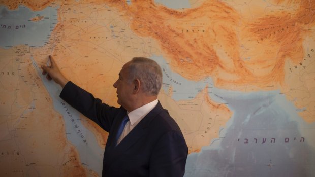 Israeli Prime Minister Benjamin Netanyahu points at Israel on the floor-to-ceiling map  of the world in his Jerusalem office.
